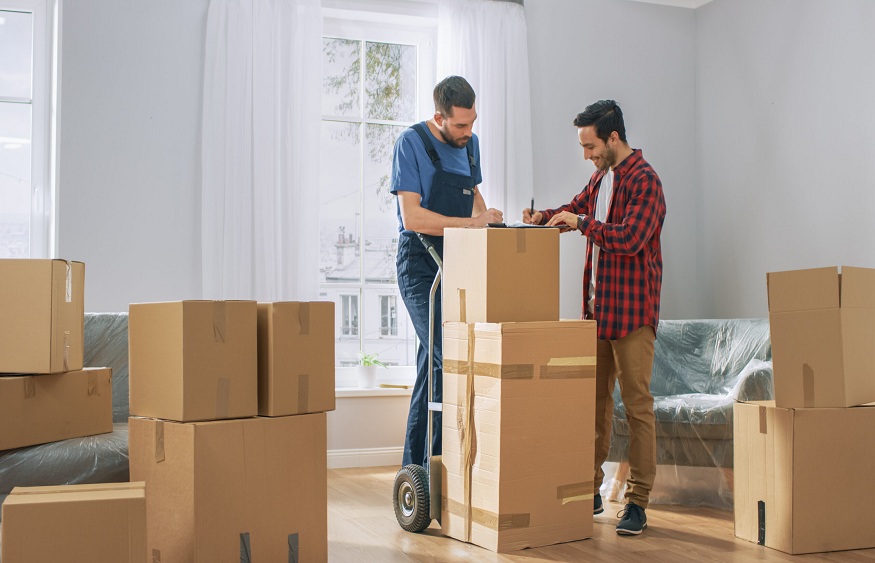 Welcomes Professional Mover with Hand Truck full of Cardboard Boxes, Receives His Goods and Signs on Clipboard.